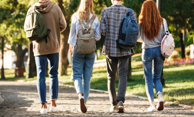 Back view group of students with backpacks walking at the campus outdoors