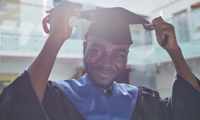 Portrait of African-American young man wearing graduation hat and smiling at camera in sunlight